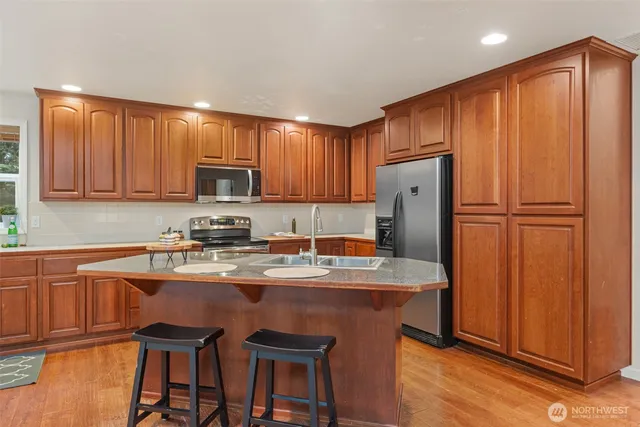 a kitchen with stainless steel appliances granite countertop a refrigerator a sink dishwasher a stove with wooden cabinets and floor