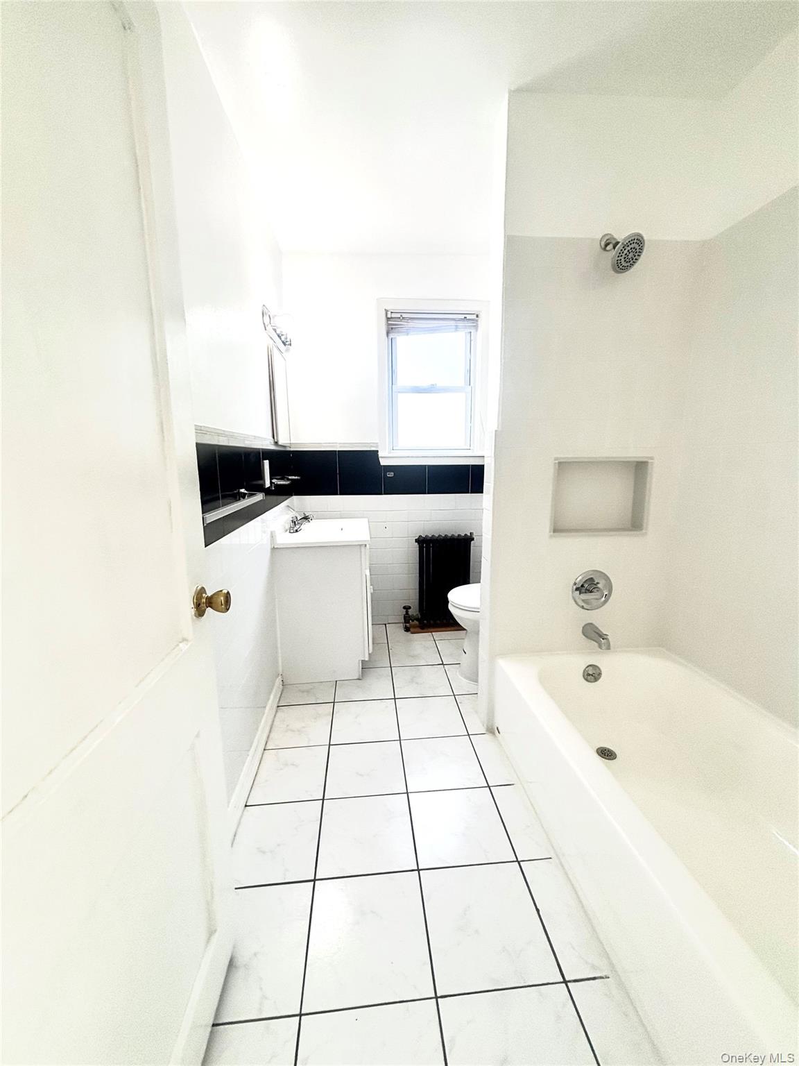 66 Kenmore Road Valley Stream, NY 11581 - Photo 6 of 15 Bathroom featuring a white bathtub with chrome fixtures, a built-in shower niche, and white tiled flooring.