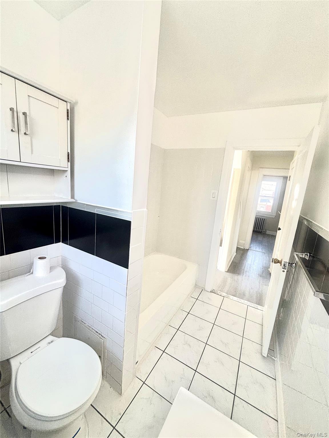 66 Kenmore Road Valley Stream, NY 11581 - Photo 7 of 15 Bathroom featuring white square tile flooring with dark grout, a white toilet, and a built-in bathtub.