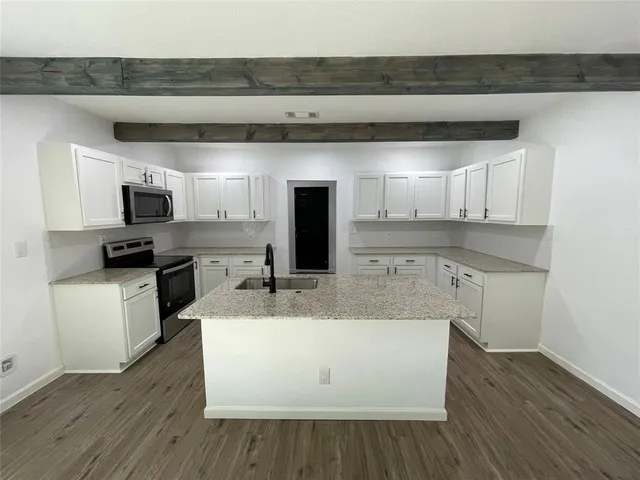 a large white kitchen with wooden floor and stainless steel appliances