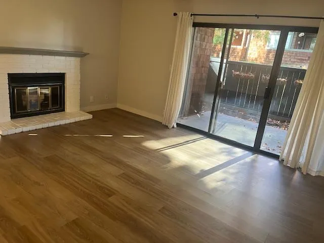 a view of an empty room with wooden floor and a fireplace