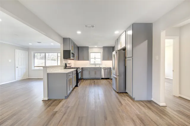 a large kitchen with a center island wooden floor stainless steel appliances and windows