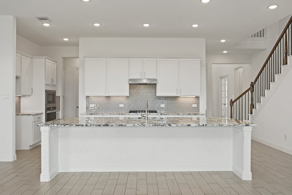 8010 Chantilly Manor Fulshear, TX 77441 - Photo 17 of 50 Spacious kitchen island with a stylish subway tile backsplash, undermount sink, ample cabinet space, gas range cooktop, and under-cabinet lighting for a modern and functional touch.