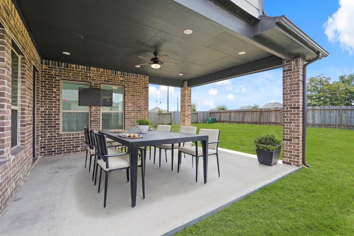 8010 Chantilly Manor Fulshear, TX 77441 - Photo 40 of 50 Spacious covered patio features stylish seating and a ceiling fan, perfect for outdoor dining and entertaining. Enjoy privacy and relaxation in the expansive backyard. Virtual staging illustrates the potential of this inviting space.