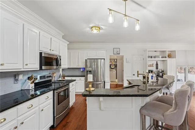 a kitchen with stainless steel appliances granite countertop a refrigerator a stove a sink a dining table and chairs with white cabinets