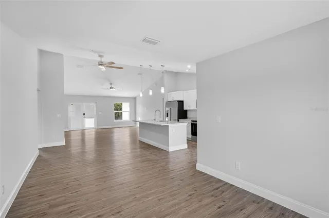 a view of an empty room and kitchen with wooden floor
