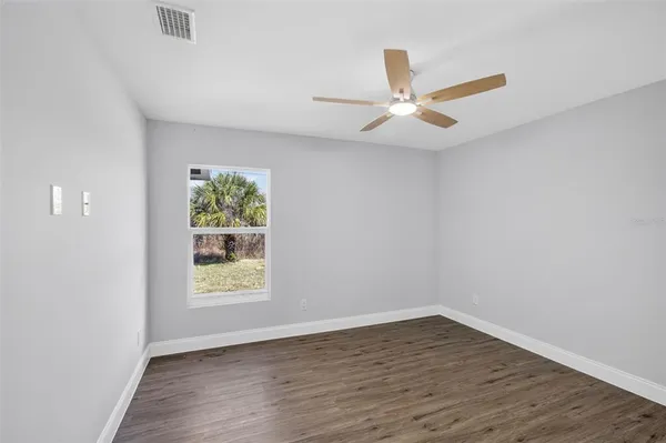 an empty room with wooden floor ceiling fan and windows