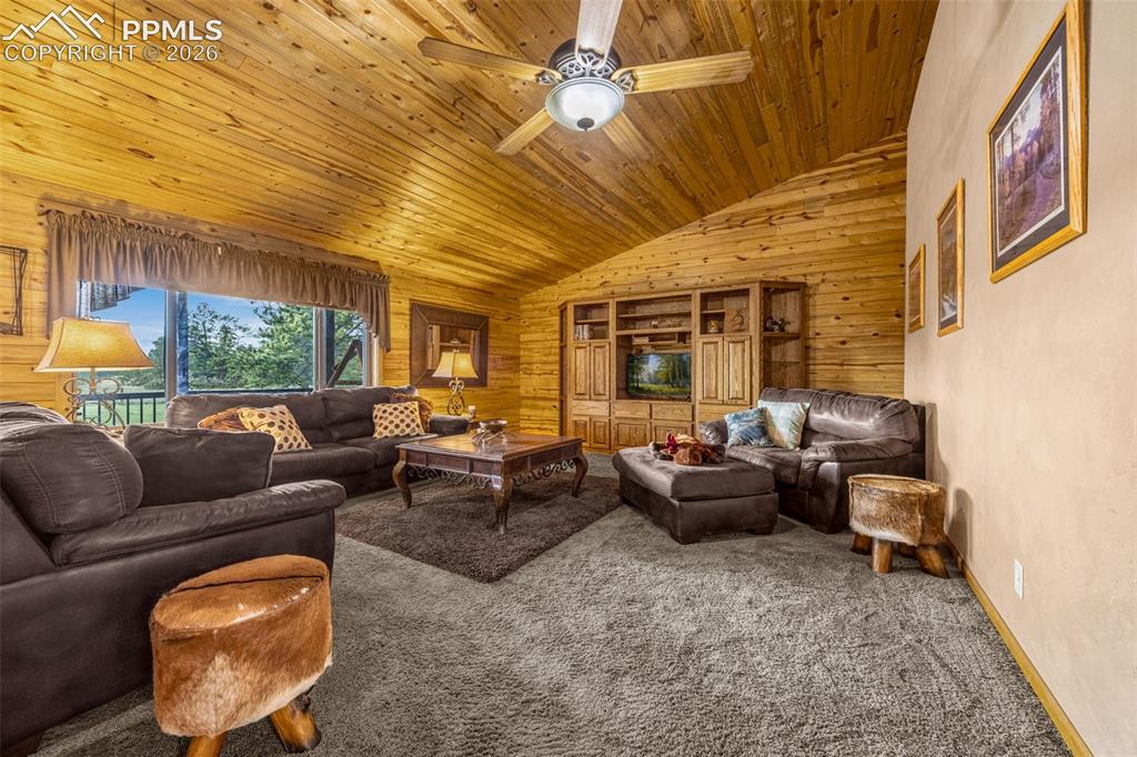 143 Ring Road Guffey, CO 80820 - Photo 5 of 36 Living room featuring wooden ceiling, carpet, vaulted ceiling, wood walls, and a ceiling fan