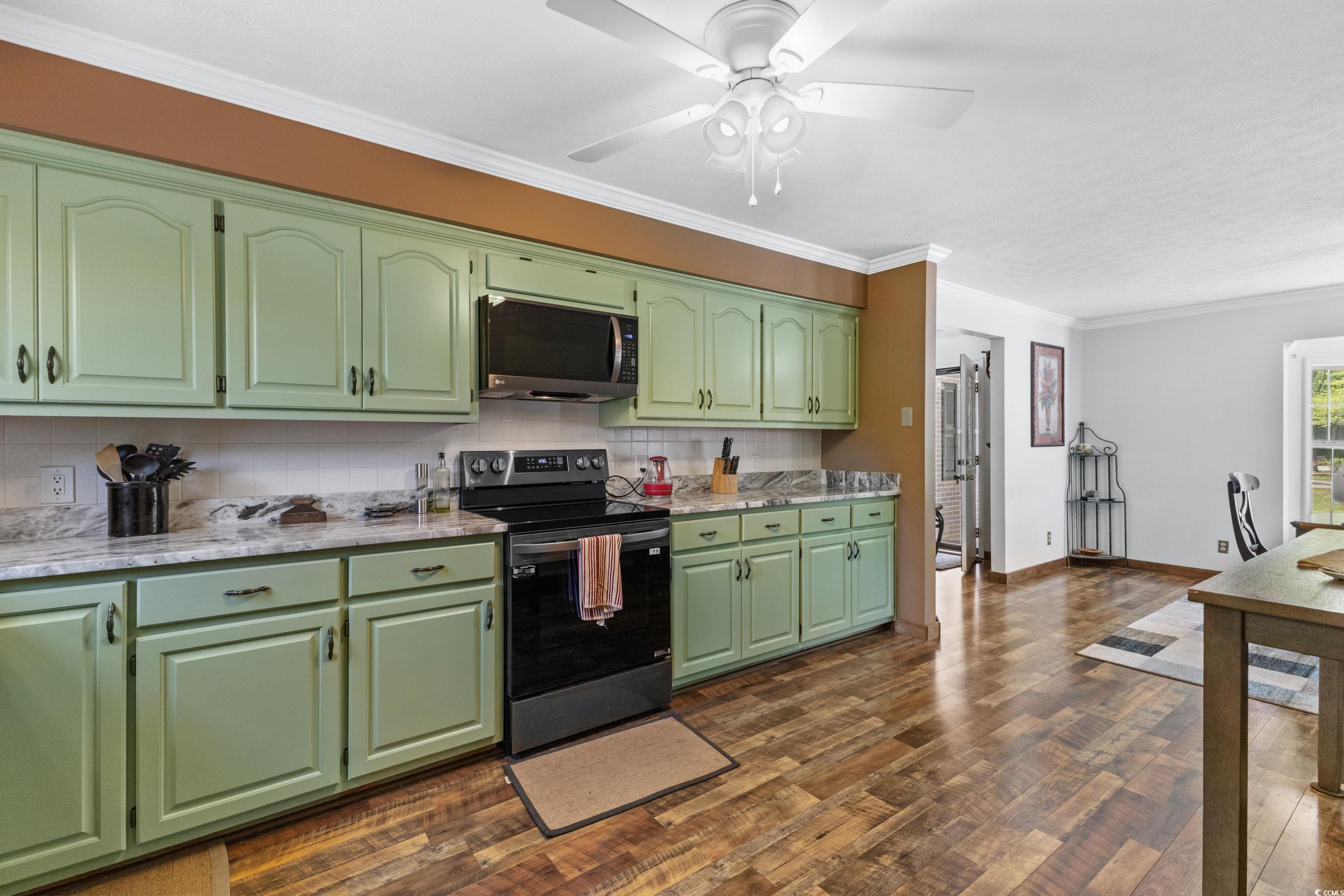 1869 Meadowood Lane Longs, SC 29568 - Photo 9 of 37 Kitchen with dark wood finished floors, black range with electric cooktop, decorative backsplash, and crown molding