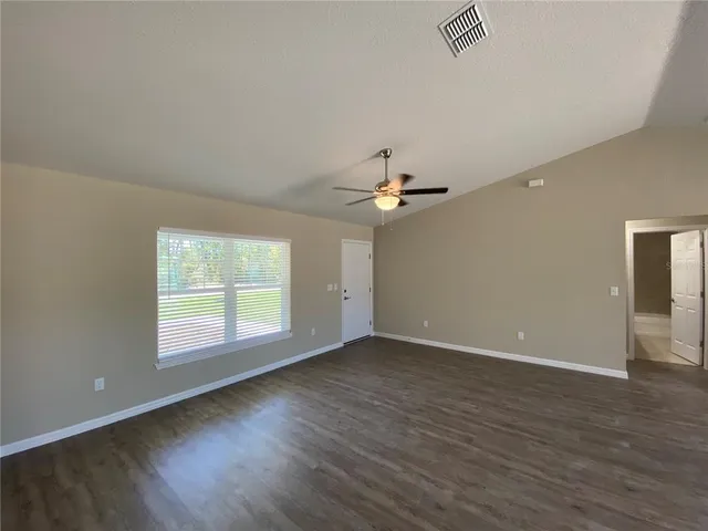 an empty room with wooden floor chandelier fan and windows