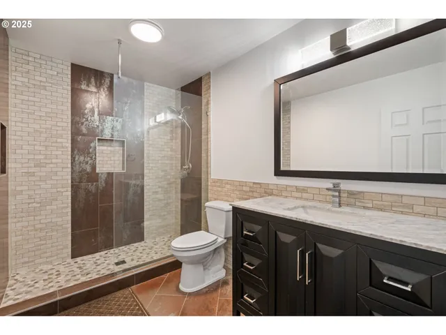 a bathroom with a granite countertop sink a toilet a mirror and shower