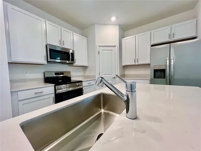 a kitchen with granite countertop a refrigerator sink and white cabinets