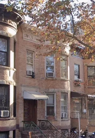 a front view of a building with yard and large trees