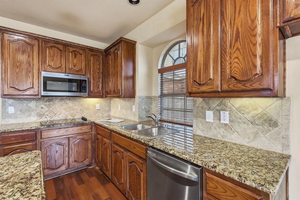 5038 West Fall Drive Midlothian, TX 76065 - Photo 17 of 40 Kitchen with light stone countertops, stainless steel appliances, dark wood finished floors, wood finish cabinetry, and tasteful backsplash