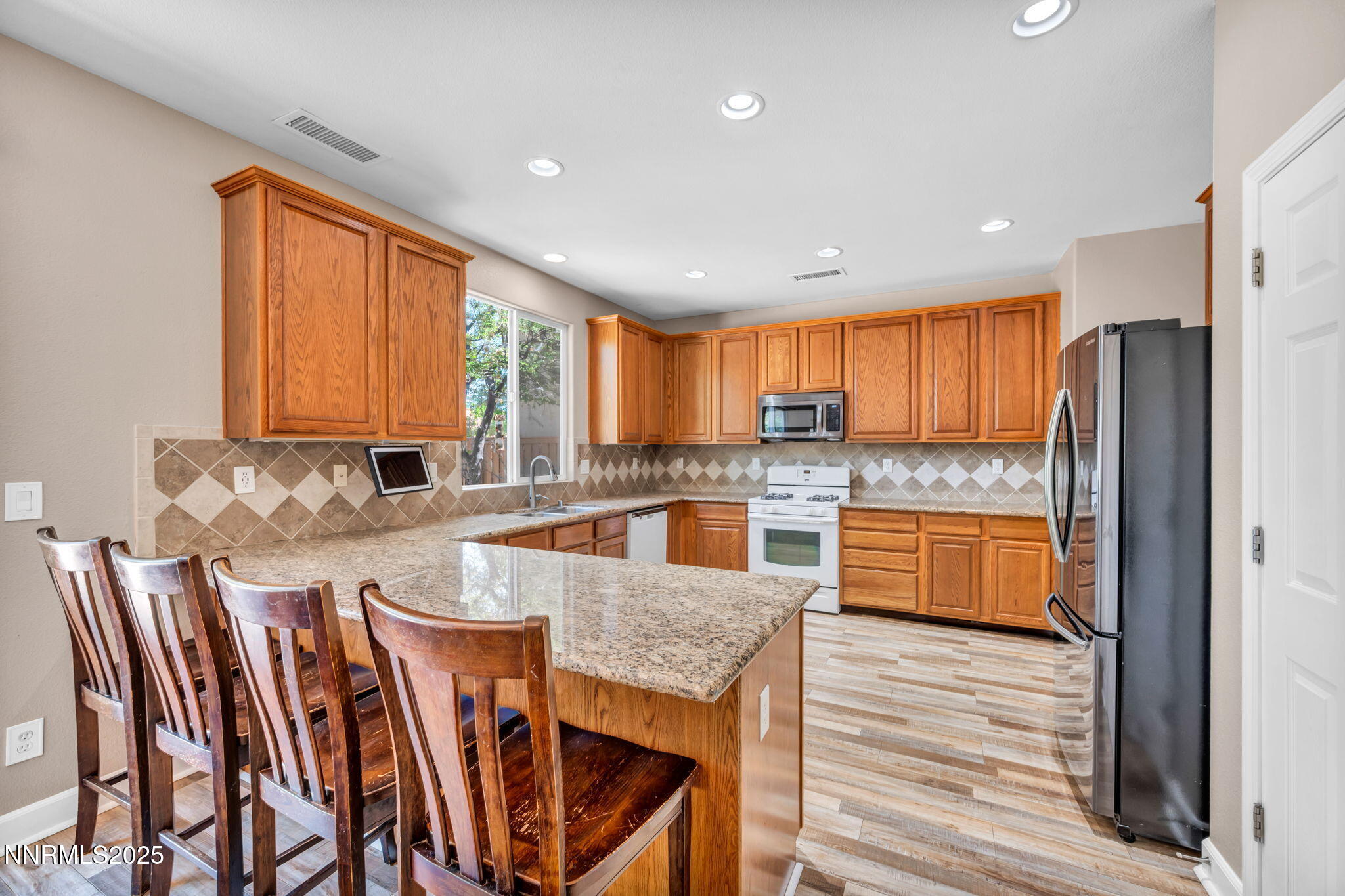 405 Sondrio Court Reno, NV 89521 - Photo 22 of 58 a large kitchen with stainless steel appliances granite countertop a refrigerator a sink dishwasher a stove and a dining table with wooden floor