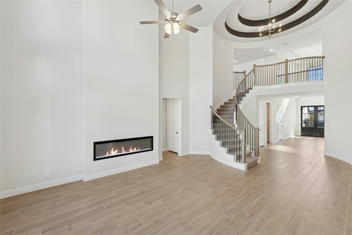 1528 Rodeo Ridge Drive Georgetown, TX 78628 - Photo 2 of 28 Unfurnished living room featuring a glass covered fireplace, light wood finished floors, stairs, a towering ceiling, and a chandelier