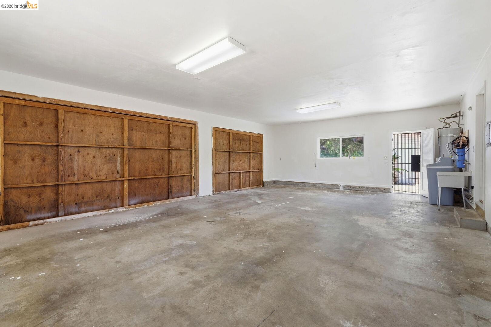 1590 Sunset Road Brentwood, CA 94513 - Photo 28 of 45 Spacious garage featuring two large wood-paneled doors, concrete flooring, overhead fluorescent lighting, and a utility sink