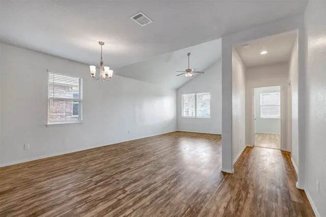 an empty room with wooden floor chandelier and windows
