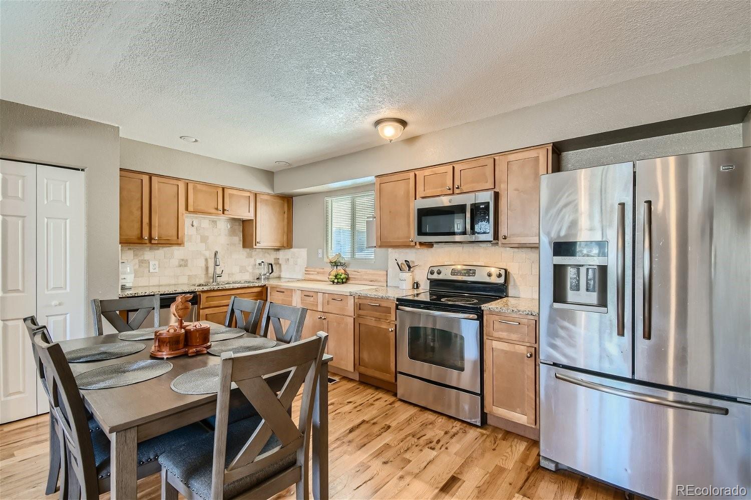 8207 High Street Denver, CO 80229 - Photo 3 of 11 a kitchen with a refrigerator a stove top oven a sink dishwasher and white cabinets with wooden floor