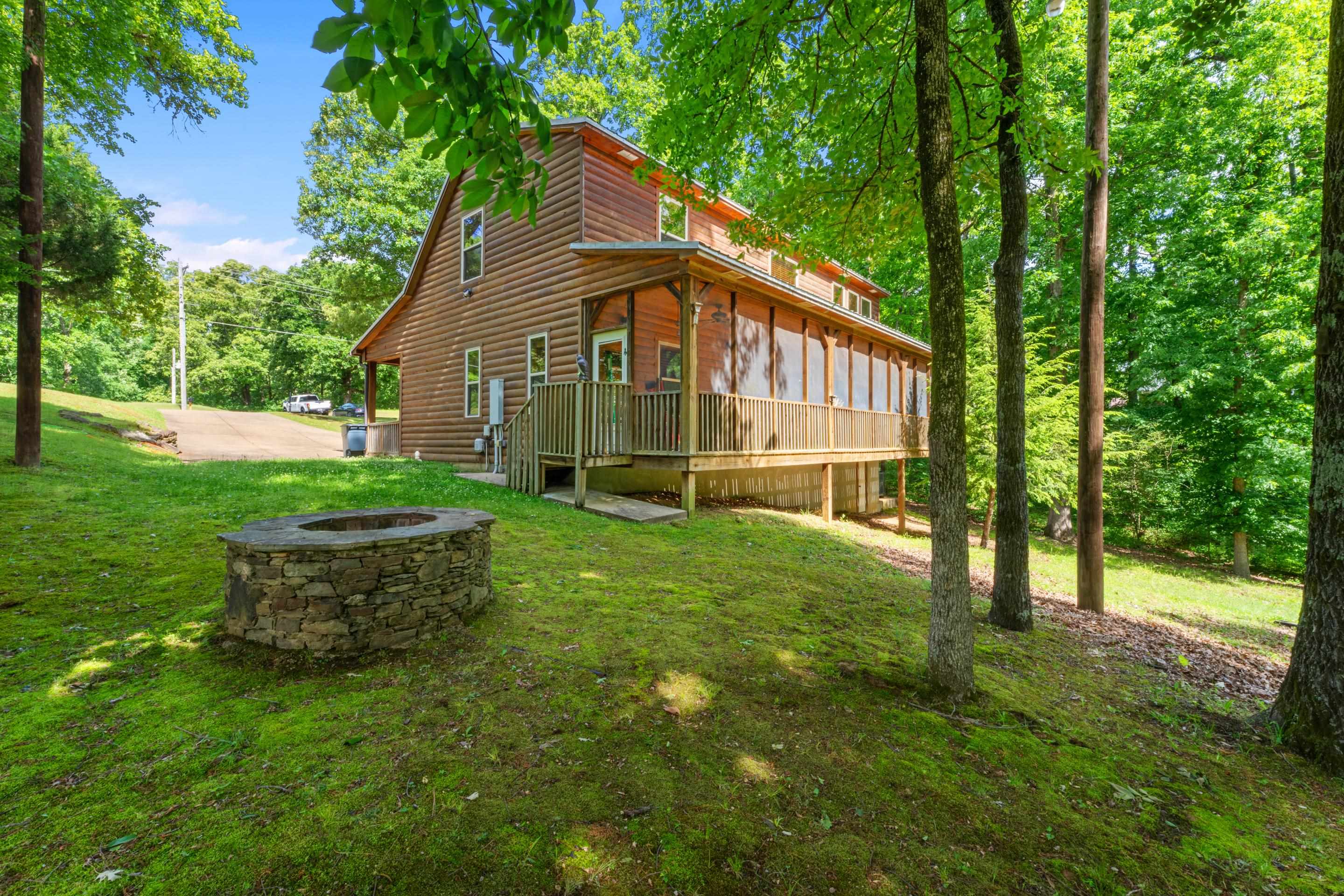 950 Cherry Road Eads, TN 38028 - Photo 26 of 30 Two-story log cabin exterior featuring a covered front porch with railings, a screened-in back porch with wood railings, a stone fire pit, and a sloped, tree-lined lawn