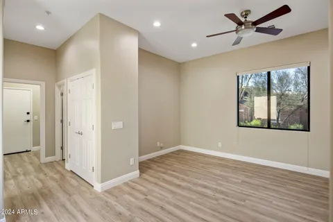 a view of an empty room with wooden floor and a ceiling fan