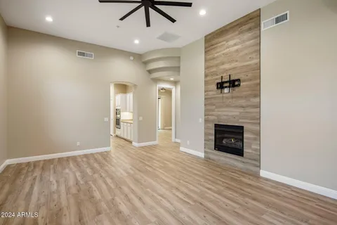 an empty room with wooden floor a ceiling fan a fireplace and windows