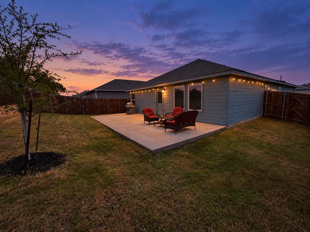 11726 Bone Spg Drive Rhome, TX 76078 - Photo 28 of 29 *Digitally Enhanced* Twilight view of the fenced backyard and extended concrete patio, highlighted by warm string lighting that creates an inviting setting for outdoor dining, relaxing, or entertaining.