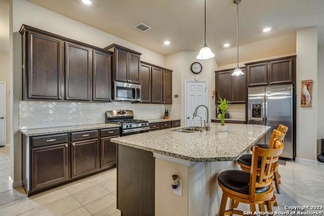 12515 Ponder Ranch San Antonio, TX 78245 - Photo 9 of 27 a kitchen with stainless steel appliances granite countertop a stove top oven a refrigerator a sink and chairs