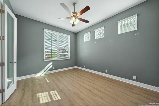 an empty room with wooden floor chandelier fan and windows