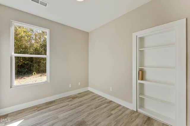 a view of an empty room with wooden floor and a window