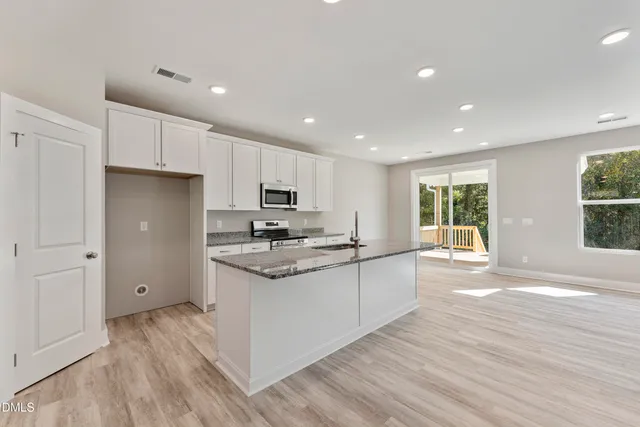 a kitchen with stainless steel appliances granite countertop a stove a sink a refrigerator and white cabinets with wooden floor