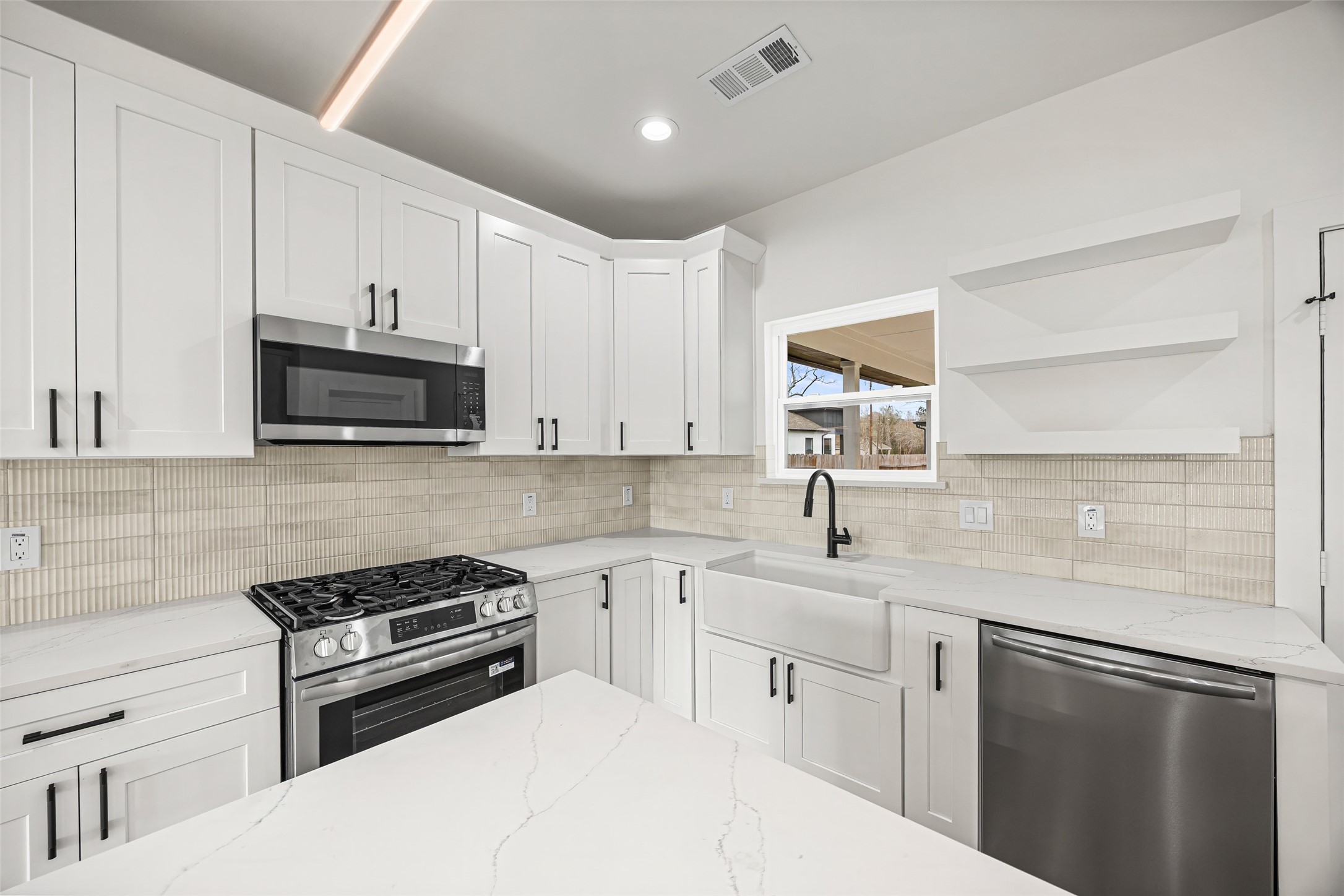 1807 Waco Street Dayton, TX 77535 - Photo 8 of 26 Shaker-style cabinetry, quartz countertops, stainless steel gas range, built-in microwave, and textured tile backsplash.