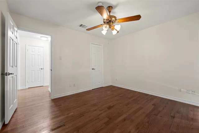 an empty room with wooden floor fan and windows