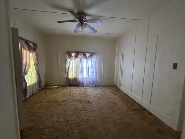 an empty room with a chandelier fan and windows