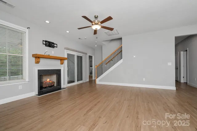 a view of an empty room with wooden floor fireplace and a window