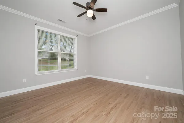 an empty room with wooden floor ceiling fan and windows