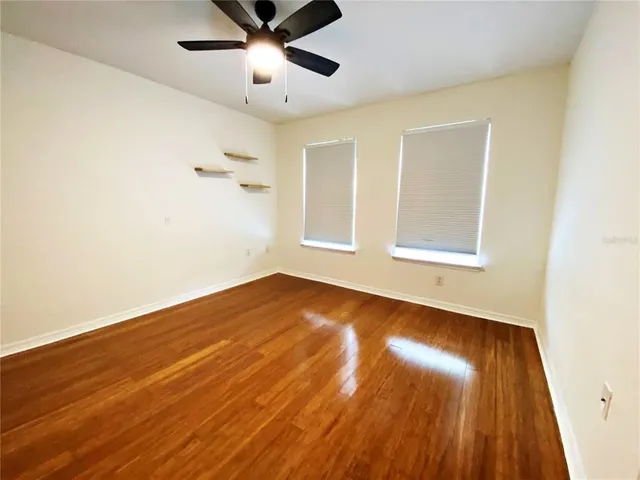 an empty room with wooden floor fan and windows