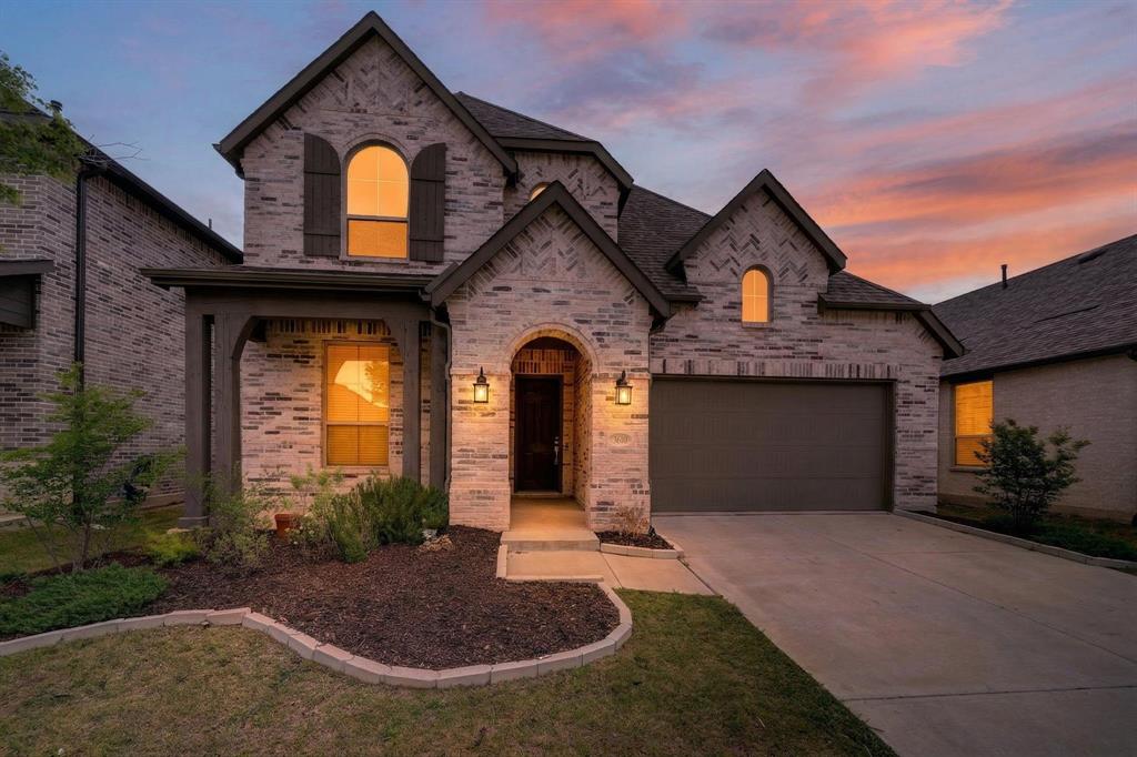 This property showcases a brick exterior with dark trim and shutters, featuring a prominent arched entry and an attached garage