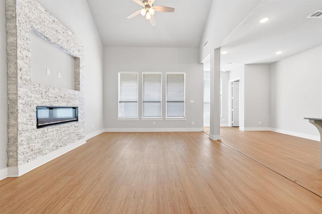 1810 Rhea Court Celina, TX 75009 - Photo 26 of 32 Spacious living area featuring light-toned flooring, a modern linear fireplace with a textured stone surround, and large windows providing natural light