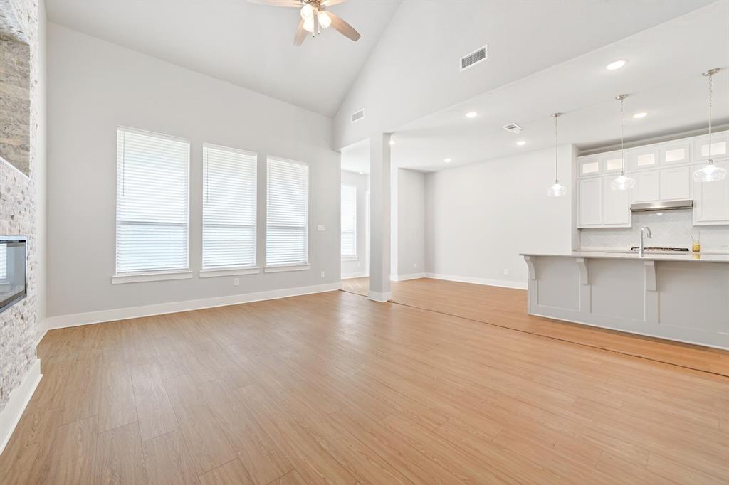 1810 Rhea Court Celina, TX 75009 - Photo 27 of 32 The property features light-colored flooring, a vaulted ceiling with a fan, and a fireplace with a stone facade
