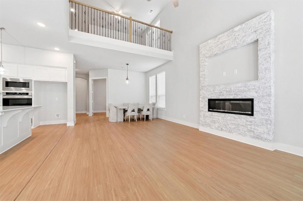1810 Rhea Court Celina, TX 75009 - Photo 29 of 32 Expansive living area with light wood flooring, a striking floor-to-ceiling fireplace featuring an electric insert and stone surround, and a kitchen island with stainless steel appliances