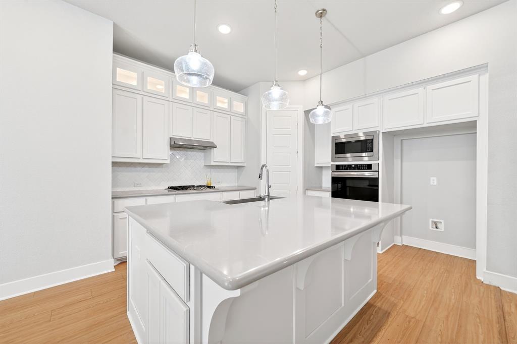1810 Rhea Court Celina, TX 75009 - Photo 30 of 32 The kitchen features a large island with a light-colored countertop, white cabinetry with upper glass-fronted sections, and light wood flooring