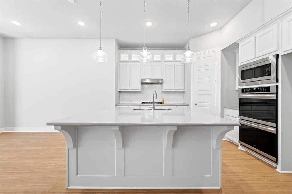 1810 Rhea Court Celina, TX 75009 - Photo 4 of 32 Kitchen featuring a large central island with a light-colored countertop, white cabinetry, and stainless steel appliances including a built-in microwave and double oven