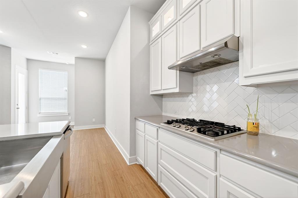 1810 Rhea Court Celina, TX 75009 - Photo 5 of 32 The kitchen features white cabinetry, a built-in gas range, a stainless steel range hood, white herringbone tile backsplash, and light-colored countertops