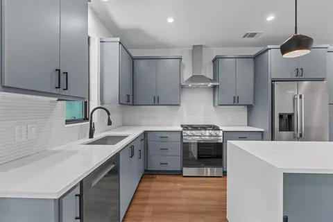 a kitchen with stainless steel appliances a refrigerator a sink a wooden floor and a potted plant