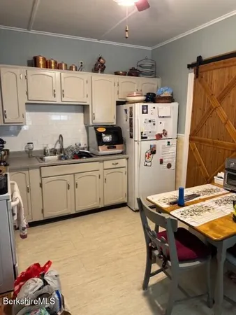 a kitchen with stainless steel appliances a white refrigerator a sink dishwasher and a dining table with wooden floor