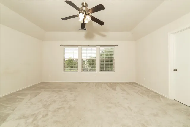 an empty room with a chandelier fan and windows