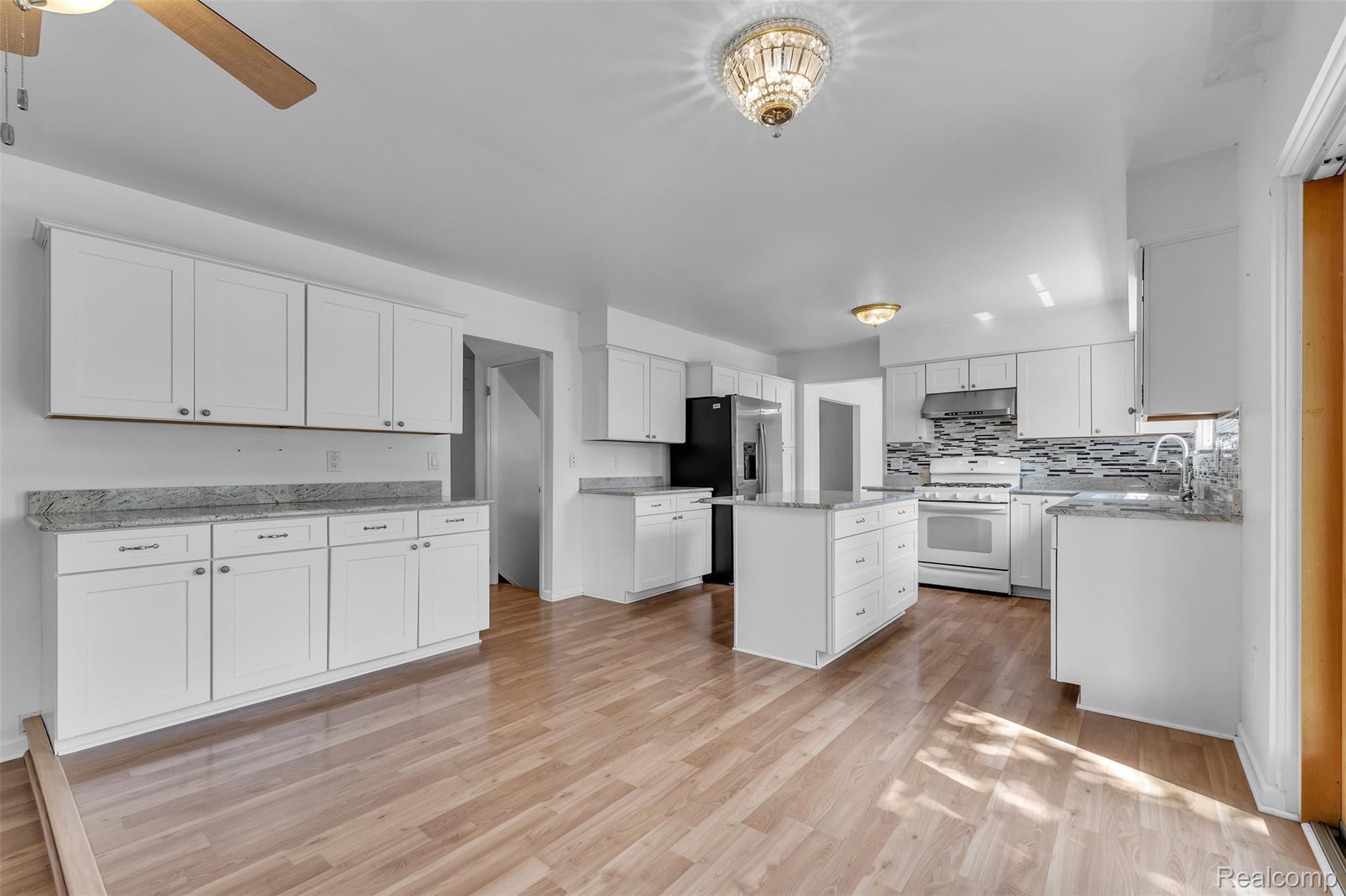 7000 Woonsocket Street Canton, MI 48187 - Photo 22 of 65 Spacious kitchen featuring light wood-finish flooring, white cabinetry, granite-style countertops, a central island, and a mosaic tile backsplash