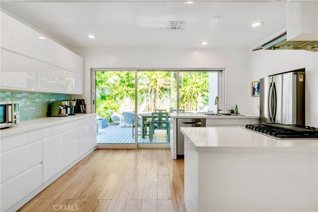 a kitchen with stainless steel appliances a large counter top a stove a chimney a sink and a refrigerator