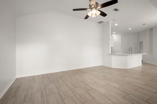 an empty room with wooden floor a ceiling fan and kitchen view
